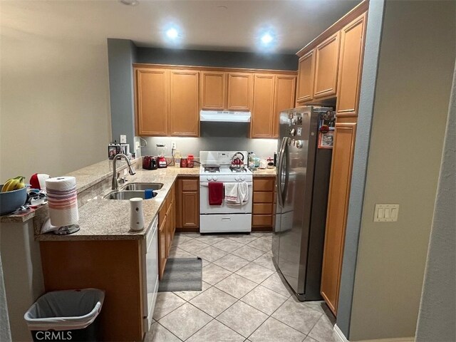 kitchen with kitchen peninsula, sink, light stone countertops, white gas stove, and stainless steel fridge