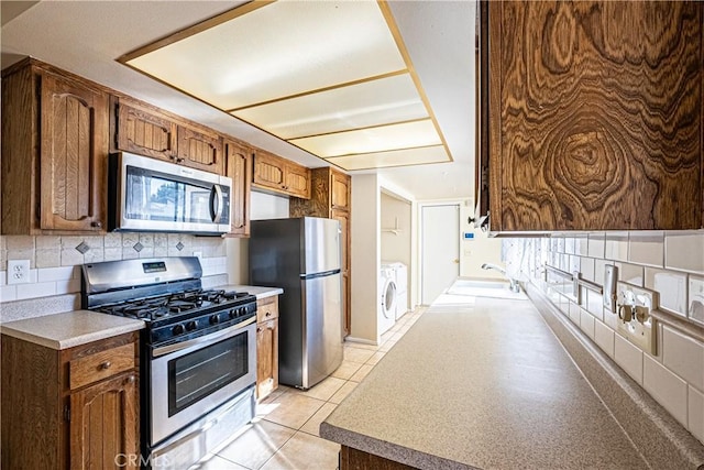 kitchen with appliances with stainless steel finishes, sink, backsplash, independent washer and dryer, and light tile patterned floors