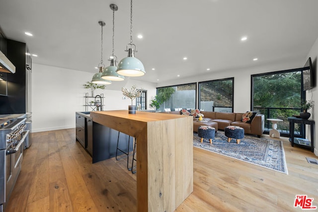 kitchen featuring a center island, sink, hanging light fixtures, stainless steel range, and light wood-type flooring