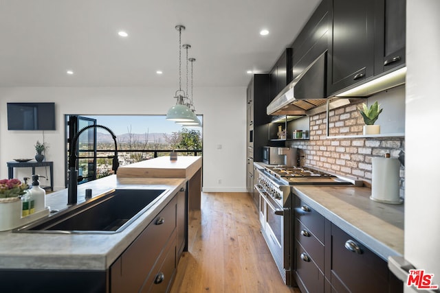 kitchen featuring light hardwood / wood-style floors, stainless steel range, decorative light fixtures, wall chimney range hood, and sink