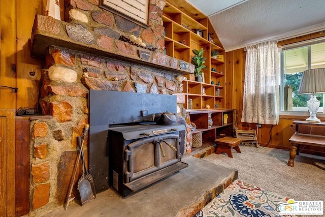 sitting room with a textured ceiling, carpet, lofted ceiling, wooden walls, and a wood stove