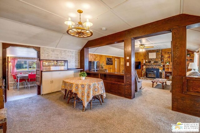 dining area with ceiling fan with notable chandelier, carpet floors, built in shelves, wooden walls, and a wood stove