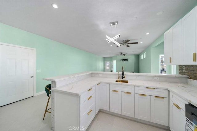 kitchen with light stone countertops, white cabinetry, a kitchen breakfast bar, sink, and kitchen peninsula