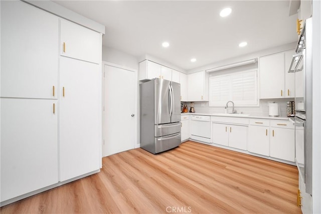 kitchen with stainless steel fridge, white dishwasher, white cabinets, light hardwood / wood-style flooring, and sink