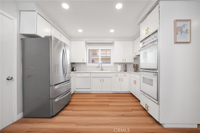 kitchen with backsplash, sink, white appliances, light wood-type flooring, and white cabinets