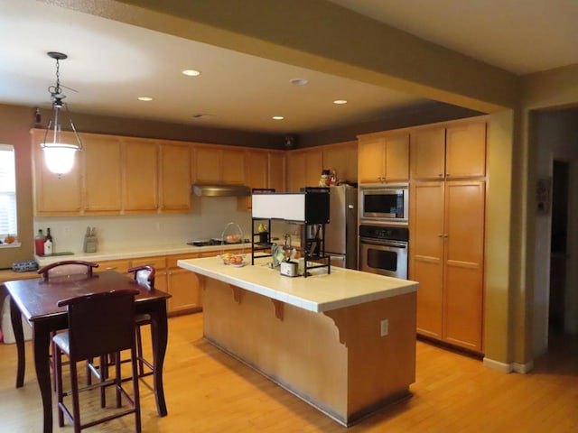 kitchen featuring an island with sink, appliances with stainless steel finishes, pendant lighting, and light wood-type flooring