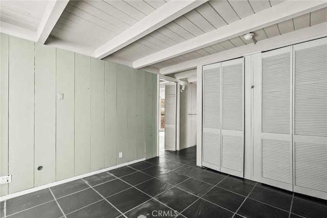 unfurnished bedroom with beam ceiling, wooden walls, and dark tile patterned floors