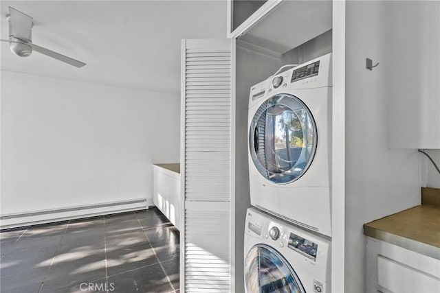 laundry room featuring ceiling fan, a baseboard radiator, dark tile patterned flooring, and stacked washing maching and dryer