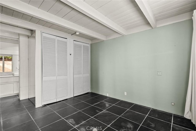 unfurnished bedroom with beam ceiling and dark tile patterned floors