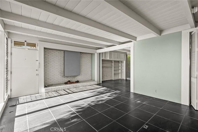 unfurnished living room with beam ceiling, plenty of natural light, brick wall, and dark tile patterned flooring