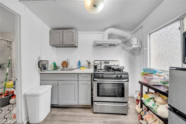 kitchen featuring sink, stainless steel range with gas stovetop, gray cabinets, light hardwood / wood-style flooring, and range hood