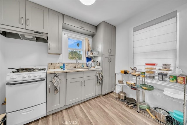 kitchen featuring white range with gas stovetop, gray cabinets, sink, and light wood-type flooring