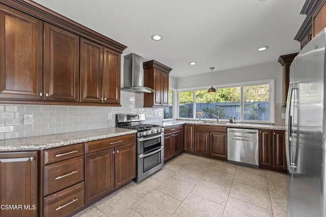 kitchen featuring pendant lighting, wall chimney range hood, stainless steel appliances, backsplash, and light stone counters