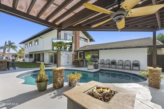 view of swimming pool with ceiling fan, an outdoor bar, a patio area, and a fire pit