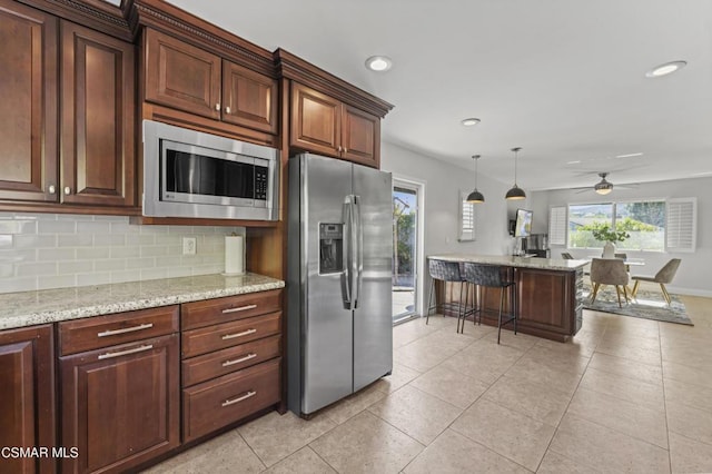 kitchen featuring ceiling fan, appliances with stainless steel finishes, backsplash, decorative light fixtures, and light stone countertops