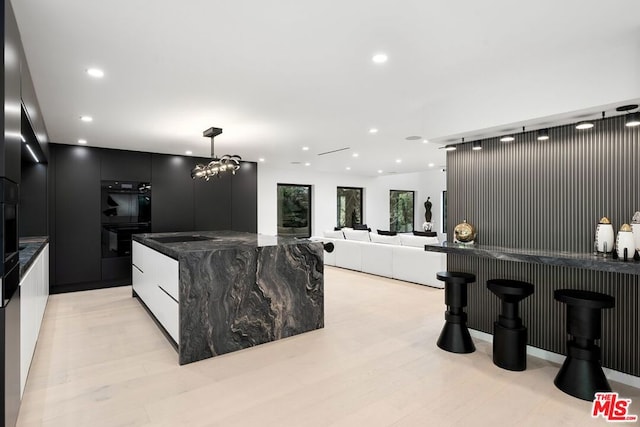 kitchen featuring double oven, light wood-type flooring, hanging light fixtures, and a kitchen island