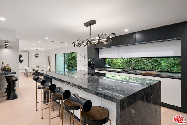 kitchen with black electric cooktop, sink, decorative light fixtures, and dark stone counters