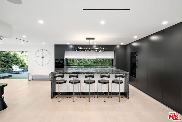 kitchen featuring decorative light fixtures, a breakfast bar area, dark stone countertops, a large island, and light wood-type flooring