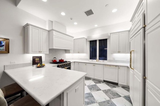 kitchen featuring high end stainless steel range oven, a kitchen bar, kitchen peninsula, and dishwasher