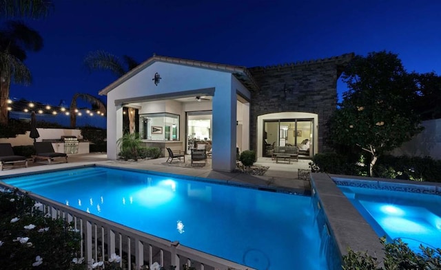 pool at twilight with an outbuilding, exterior kitchen, a patio area, and ceiling fan