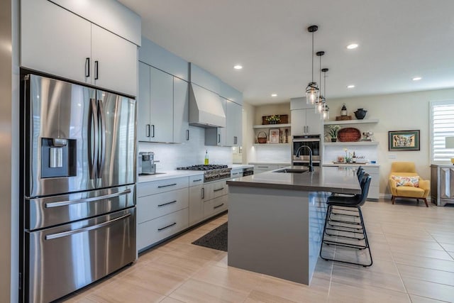 kitchen with premium range hood, stainless steel appliances, a kitchen island with sink, a kitchen breakfast bar, and hanging light fixtures