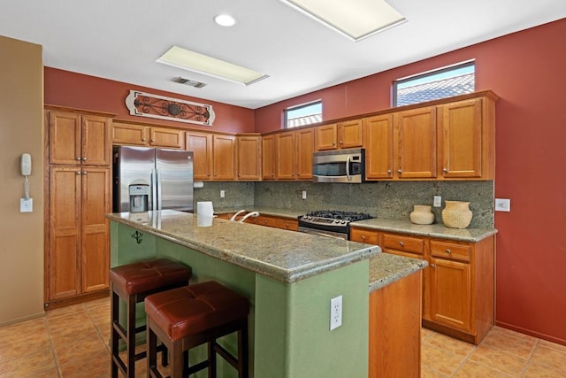 kitchen featuring a breakfast bar area, appliances with stainless steel finishes, light stone counters, and a kitchen island with sink