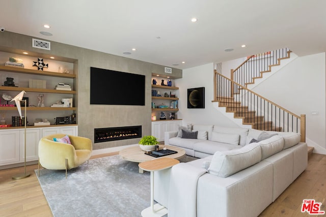 living room with a fireplace, light wood-type flooring, and built in features