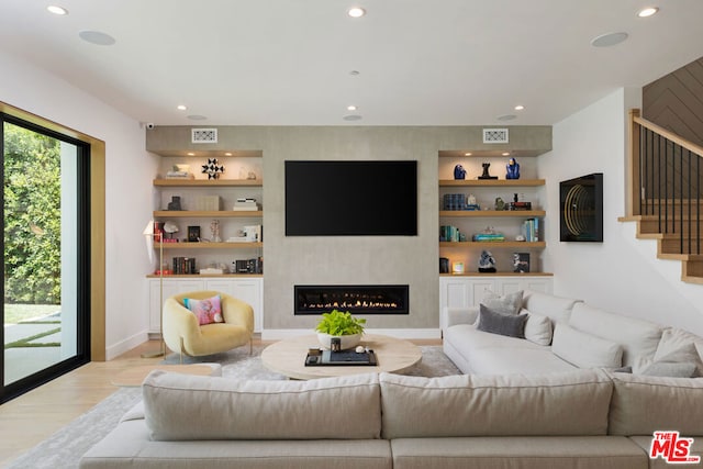 living room featuring a large fireplace, built in shelves, and light hardwood / wood-style flooring