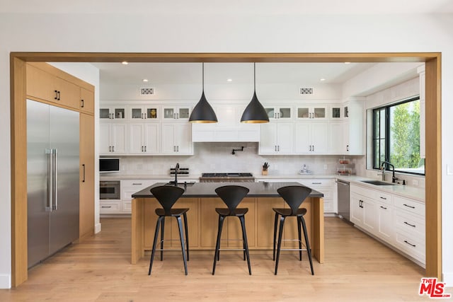 kitchen featuring white cabinetry, a kitchen bar, an island with sink, appliances with stainless steel finishes, and decorative backsplash