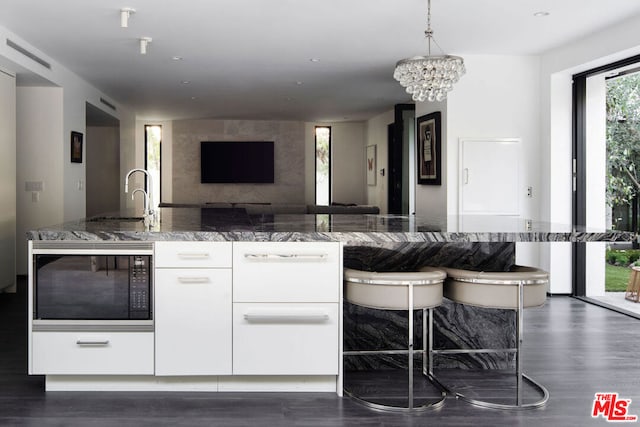 kitchen featuring a chandelier, sink, built in microwave, white cabinets, and stone countertops