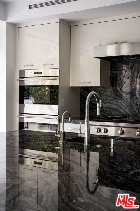 kitchen featuring white cabinetry, backsplash, and stainless steel double oven