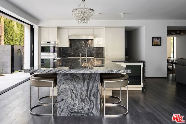 kitchen with pendant lighting, white cabinets, dark hardwood / wood-style flooring, dark stone counters, and backsplash