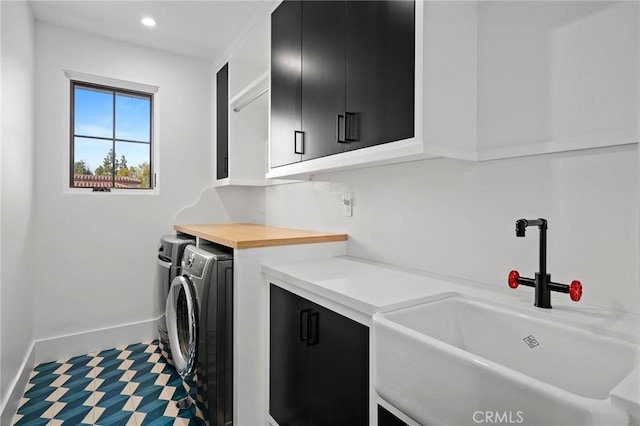 clothes washing area featuring sink, washing machine and clothes dryer, and cabinets