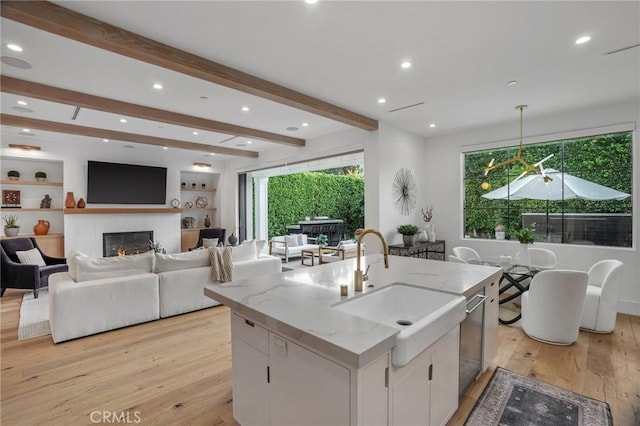 kitchen featuring decorative light fixtures, light stone counters, white cabinets, and an island with sink