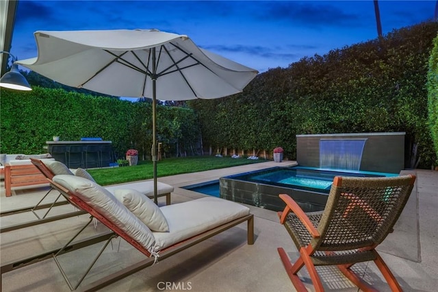 pool at dusk featuring a patio and an in ground hot tub