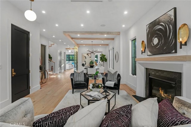 living room with a tile fireplace, beamed ceiling, and light wood-type flooring