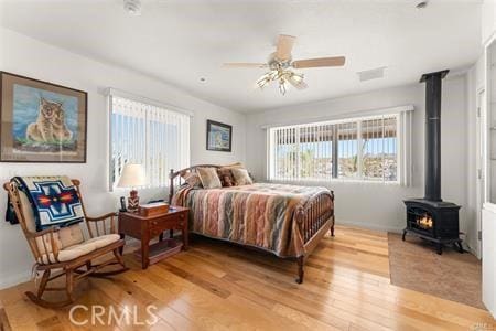 bedroom featuring light wood-type flooring, ceiling fan, and a wood stove