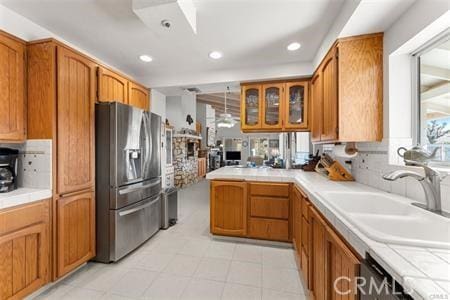 kitchen with tile countertops, kitchen peninsula, sink, stainless steel fridge with ice dispenser, and dishwashing machine