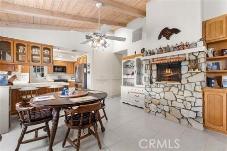 dining area featuring ceiling fan, wood ceiling, a stone fireplace, and lofted ceiling with beams