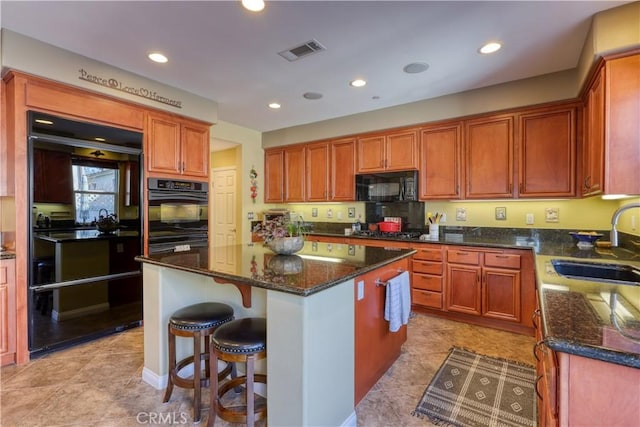 kitchen with visible vents, dark stone countertops, a center island, black appliances, and a sink