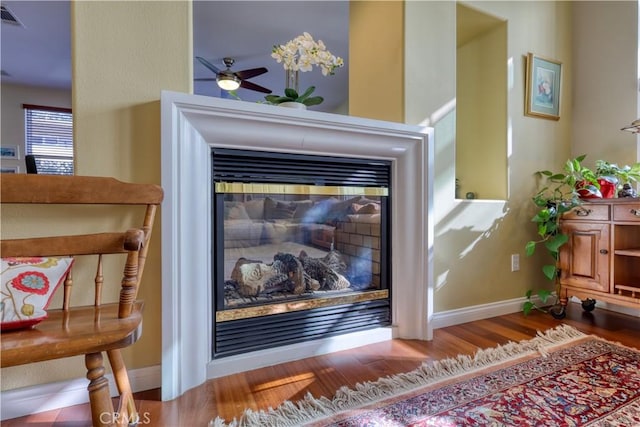 room details with wood finished floors, a ceiling fan, visible vents, baseboards, and a glass covered fireplace