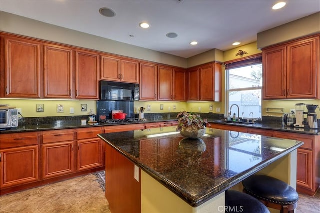 kitchen with dark stone counters, a center island, stainless steel gas stovetop, black microwave, and a sink