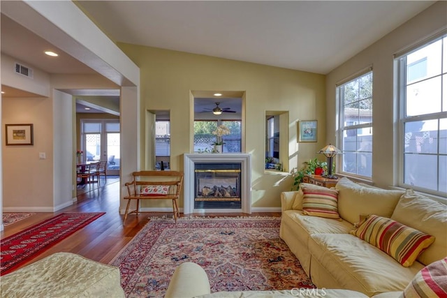 living area with vaulted ceiling, a glass covered fireplace, wood finished floors, and baseboards