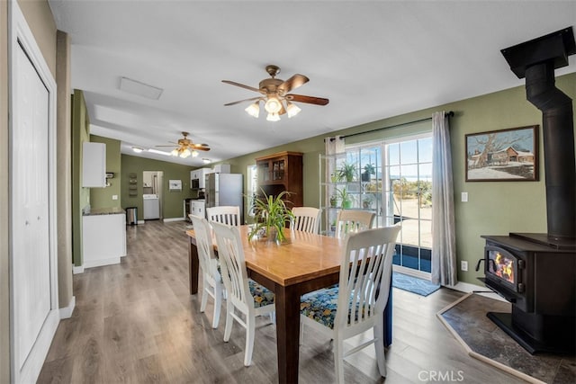 dining area featuring light wood-type flooring, ceiling fan, vaulted ceiling, and a wood stove