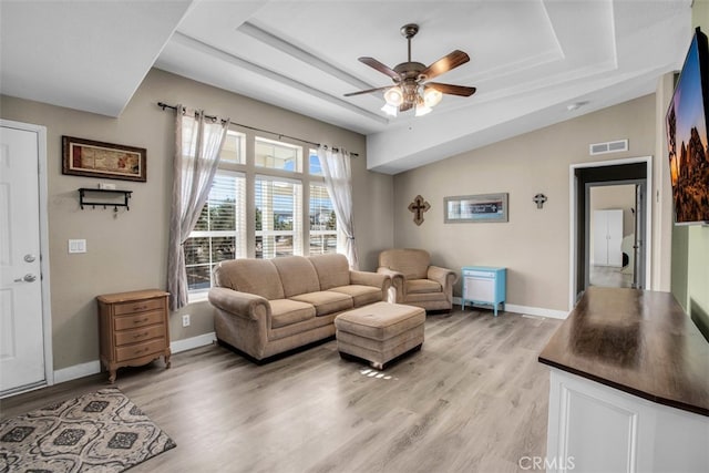 living room with ceiling fan, a tray ceiling, and light hardwood / wood-style flooring