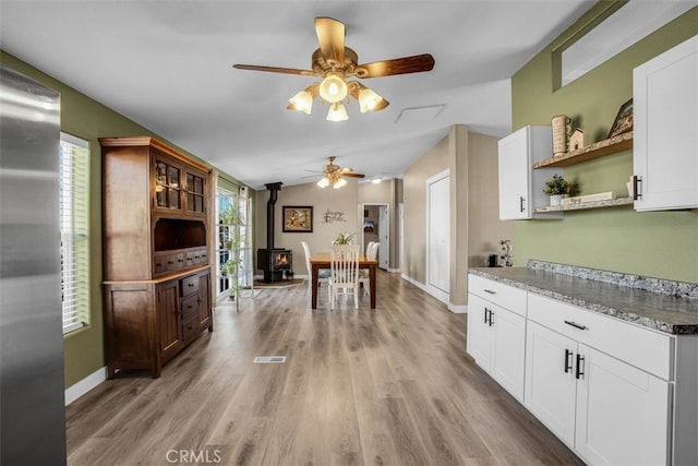 kitchen featuring light hardwood / wood-style flooring, ceiling fan, a wood stove, and white cabinets