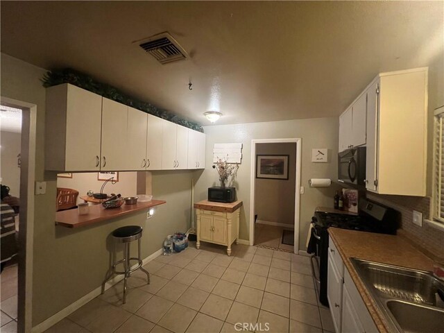 kitchen with range with gas cooktop, light tile patterned floors, sink, and white cabinetry