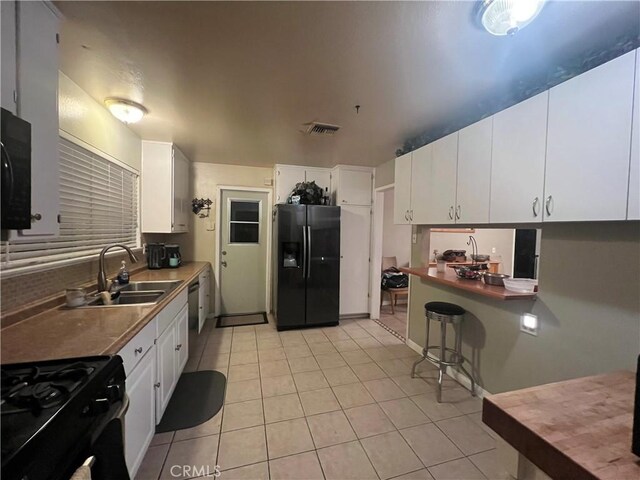 kitchen with sink, white cabinetry, light tile patterned floors, and black appliances