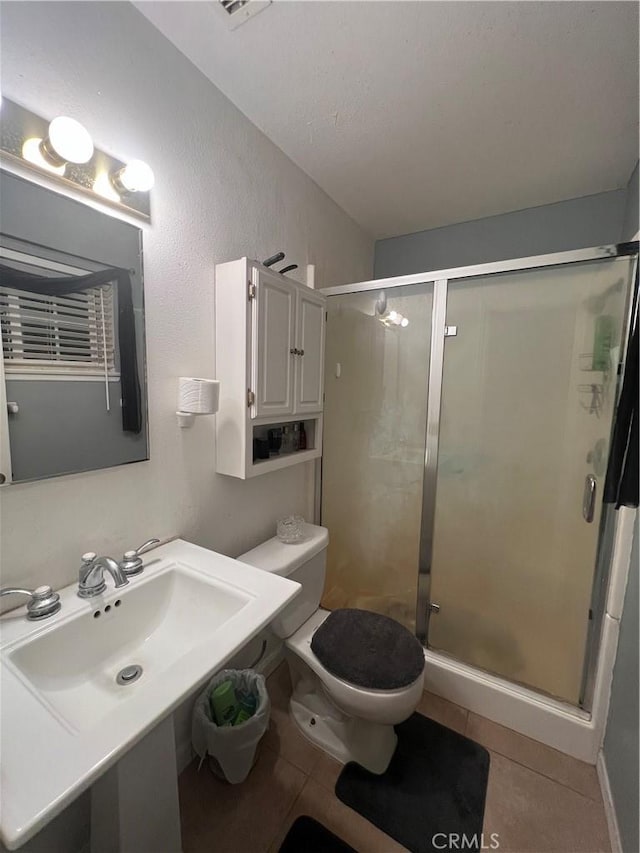 bathroom with sink, toilet, an enclosed shower, and tile patterned flooring