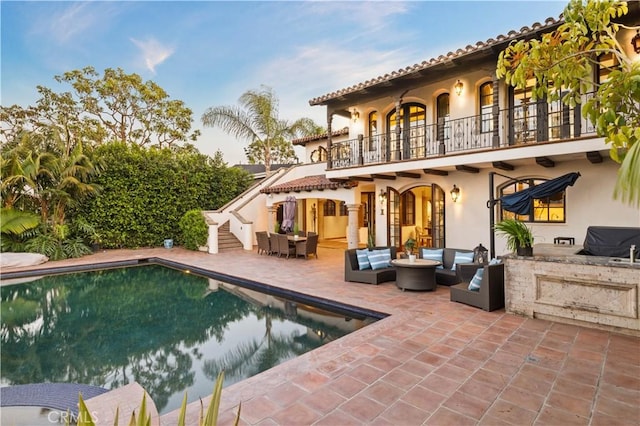 rear view of property featuring a balcony, outdoor lounge area, a patio, and exterior bar